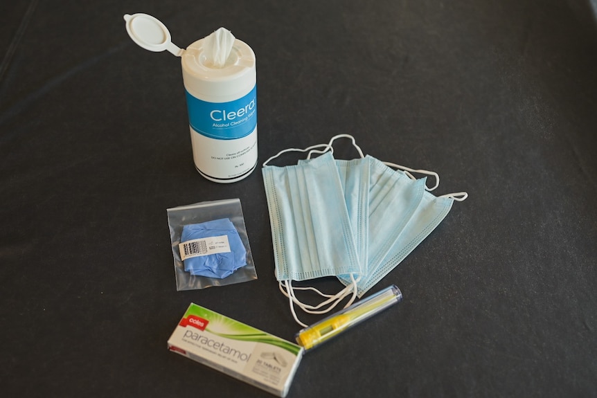 Bottle of sanitising wipes, masks, rapid antigen test kit on a table.