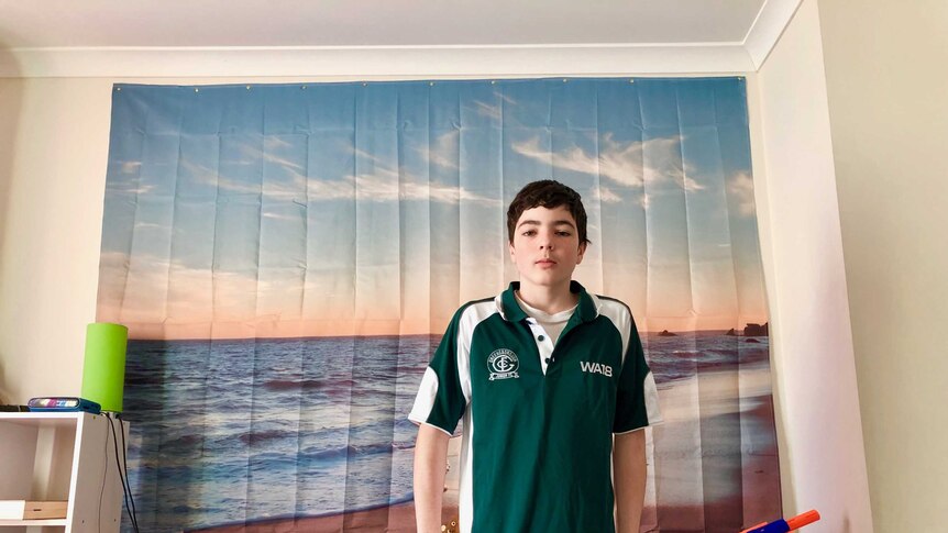 Eden in his bedroom, standing from of a beach scene on cloth pinned to his wall