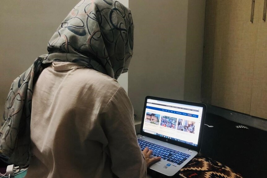 A young woman wearing a headscarf peers over a laptop