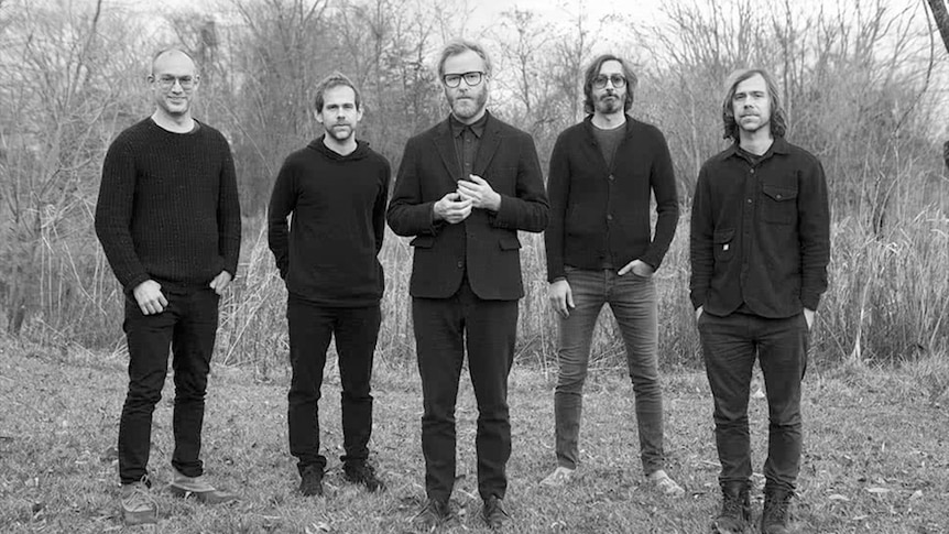 Black and white image of The National in a forest dressed in black