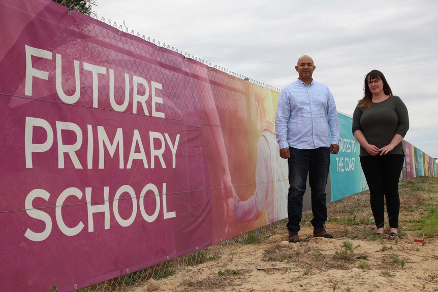A man and woman stand next to a fence with a sign that says "future primary school" on it.