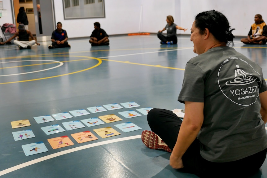 A woman sitting on the floor with yoga cards on the floor in front of her. 