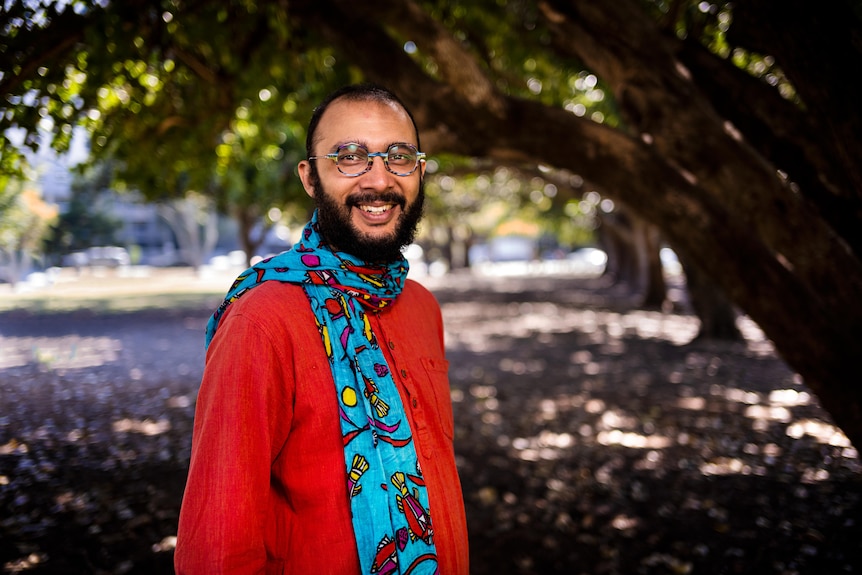 Smiling Jonathan Sriranganathan wearing red clothing and a scarf while standing in front of trees.