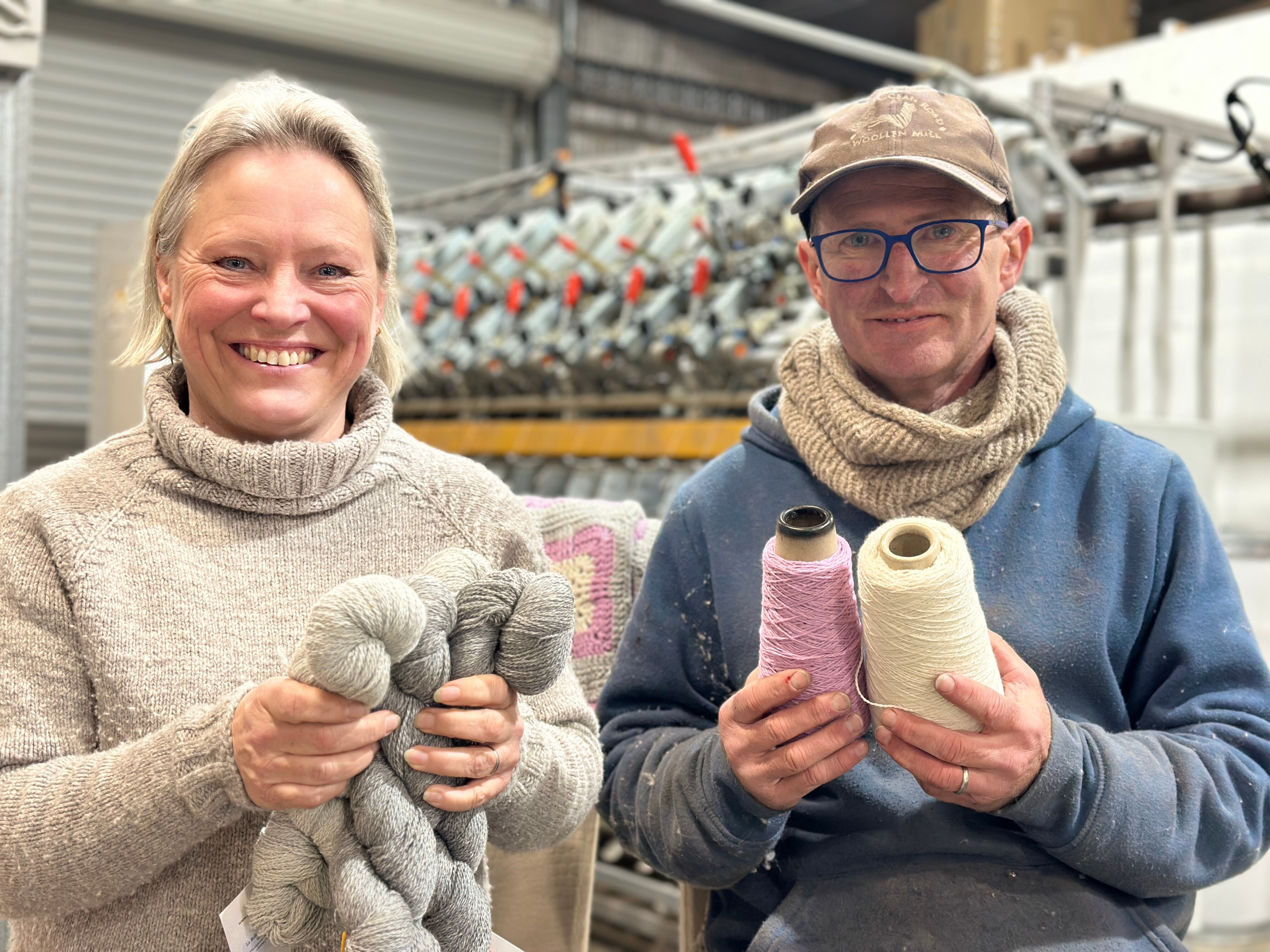 A woman and man smile as they hold wool.
