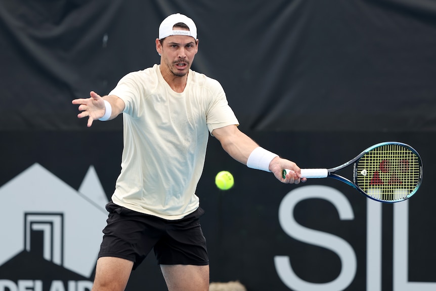 A male tennis player spreads his arms wide as prepared to hit an approaching ball.