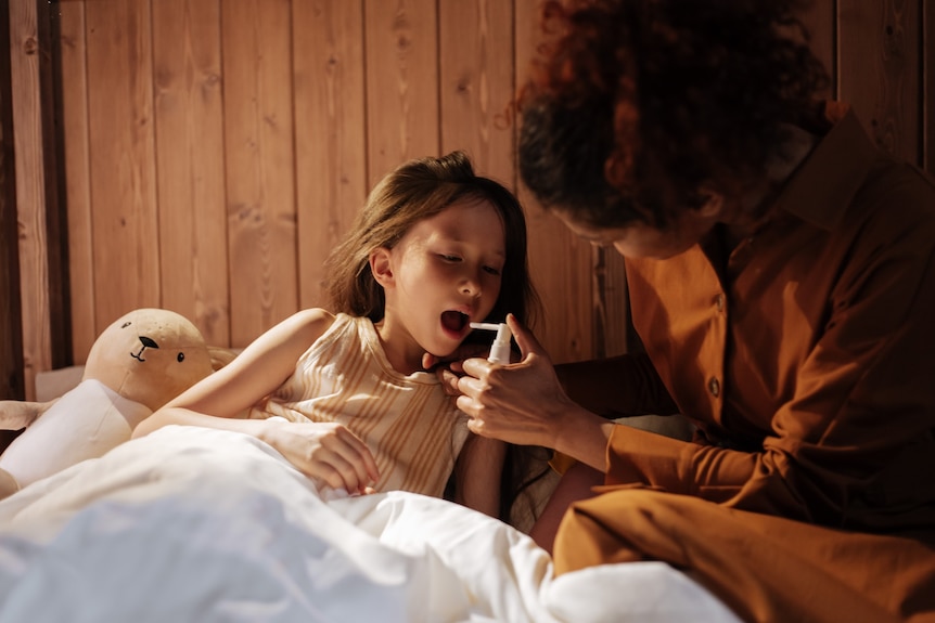 A woman giving a child throat spray in bed