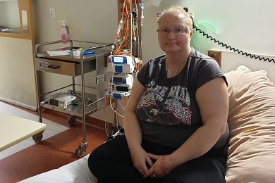 A woman sitting with crossed legs on a hospital bed.
