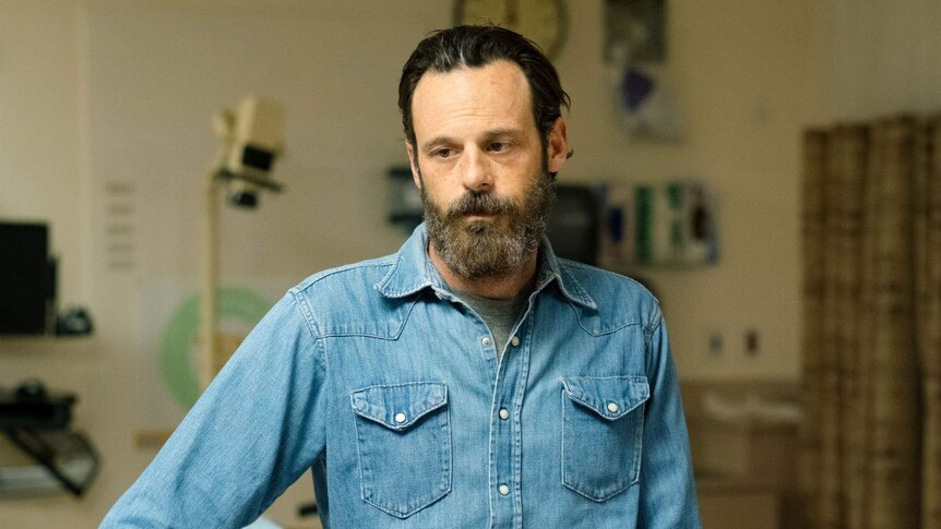 The actor, bearded and wearing a denim shirt and a beard, looks desolate in a hospital ward.