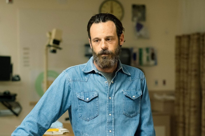 The actor, bearded and wearing a denim shirt and a beard, looks desolate in a hospital ward.