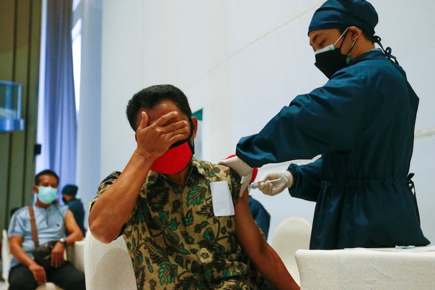 A man with his hand over his eyes gets a needle from a doctor. 