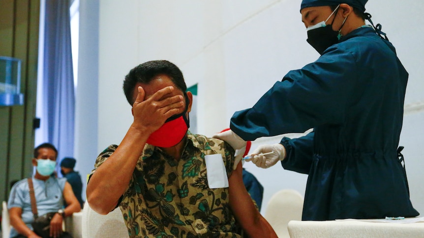 A man with his hand over his eyes gets a needle from a doctor. 