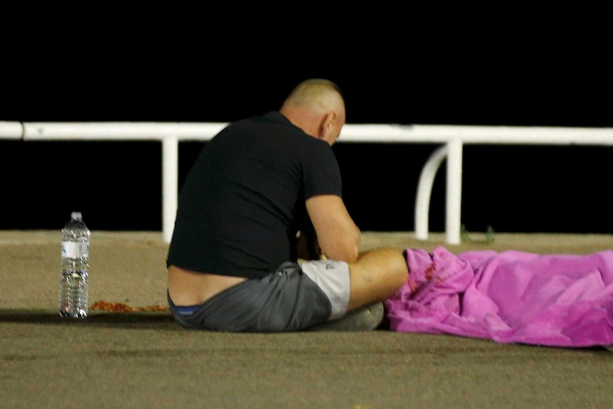 A man waits by the body of a victim of the Nice attack