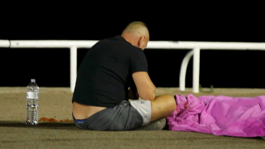 A man waits by the body of a victim of the Nice attack
