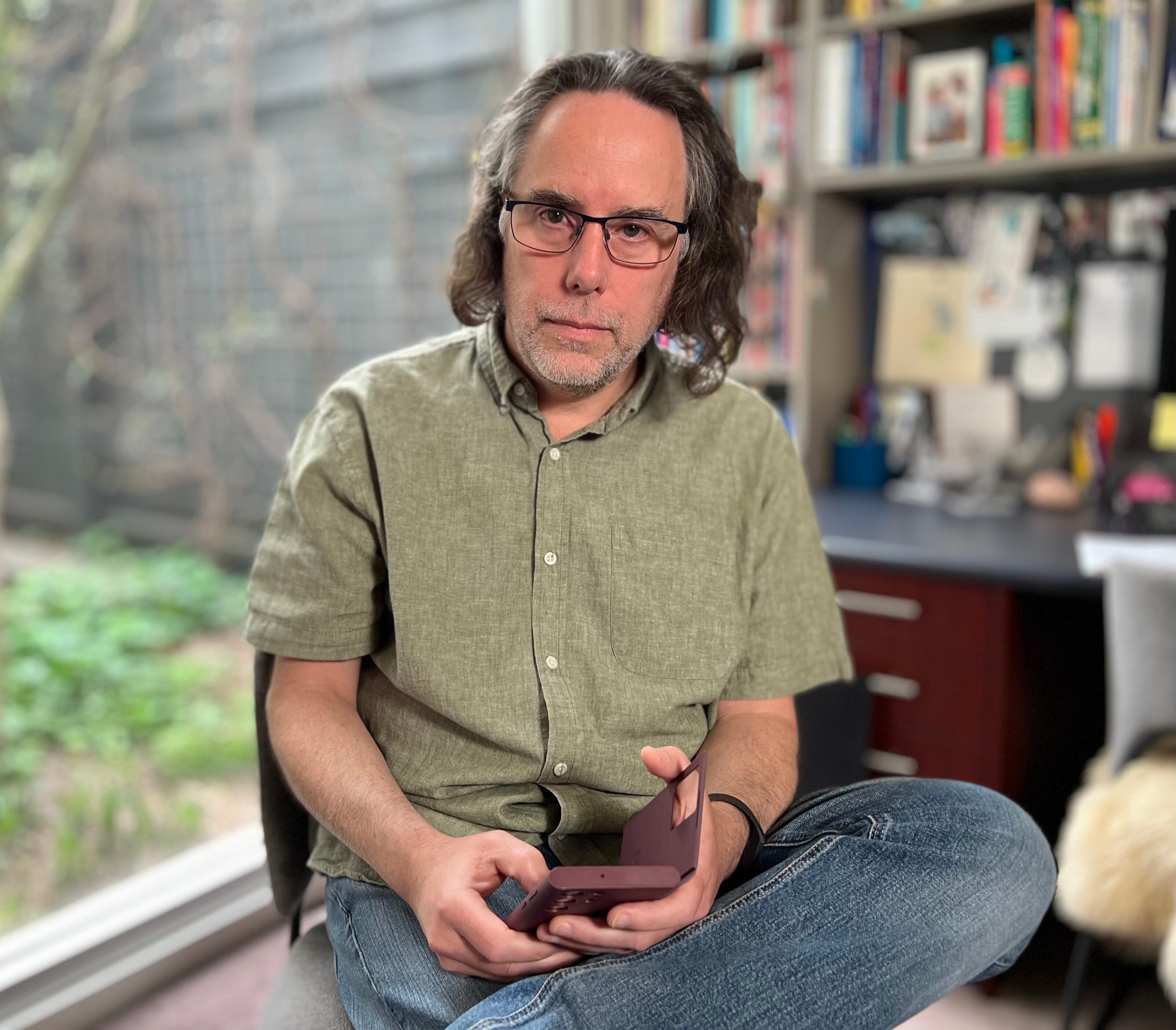 A man looks at the camera, with his phone in hand.