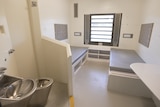 A small room with two bare single beds on either side, with a stainless steel basin and toilet in the foreground.