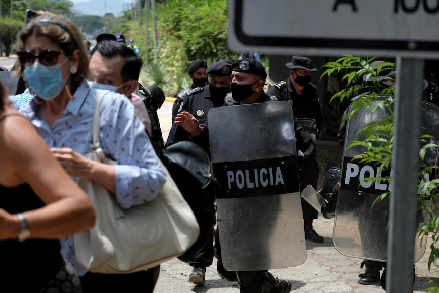 Police in black riot gear force journalists away from a home