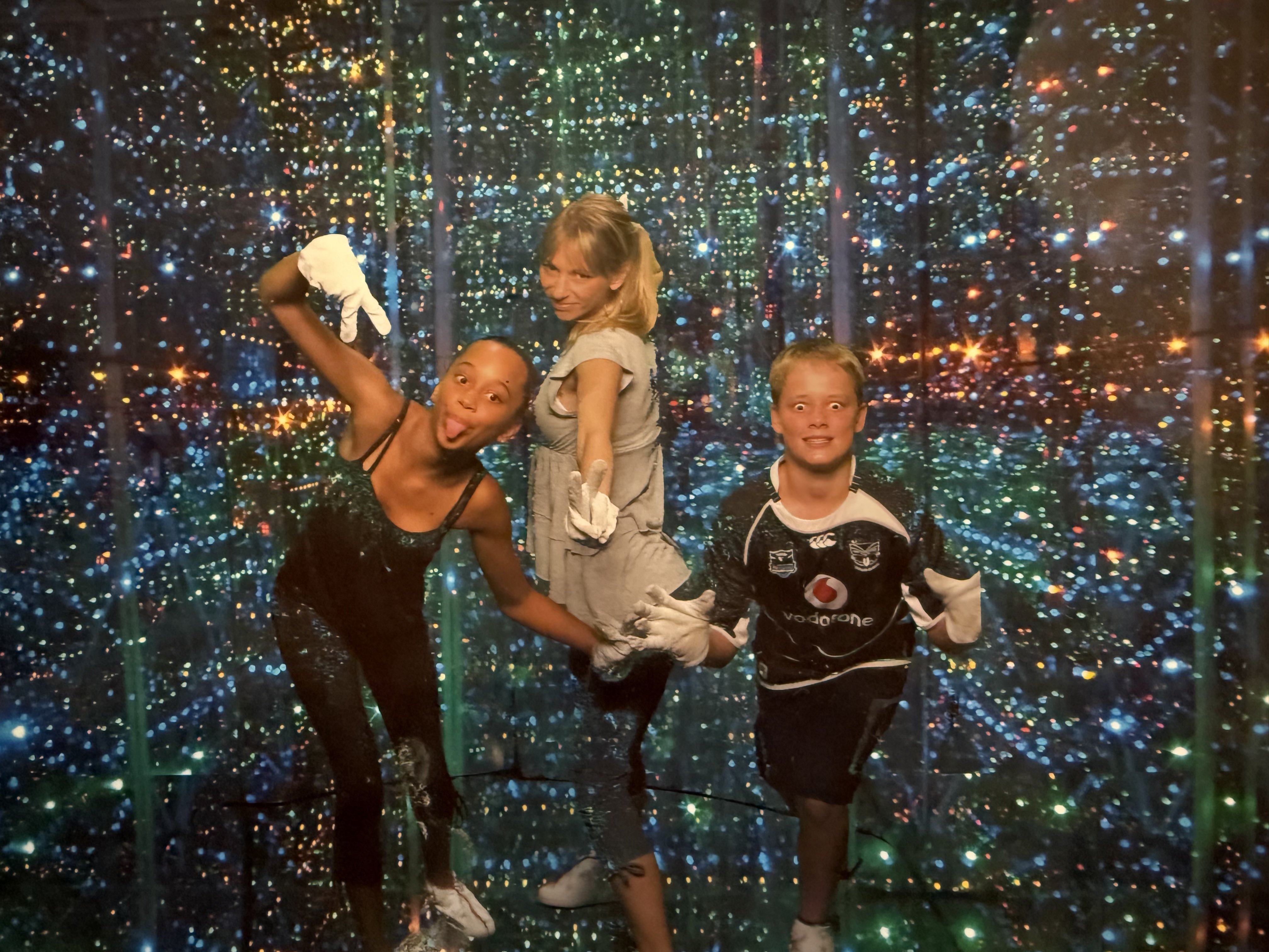Three children posing for the camera in a light-filled sensory room at a theme park.