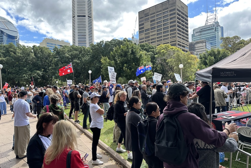 A crowd of people gathered around some Australian flags flying and posters held up 