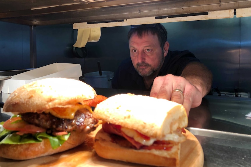 Brisbane restaurateur Sandro Romano preparing food. He reaches into the pass towards two sandwiches