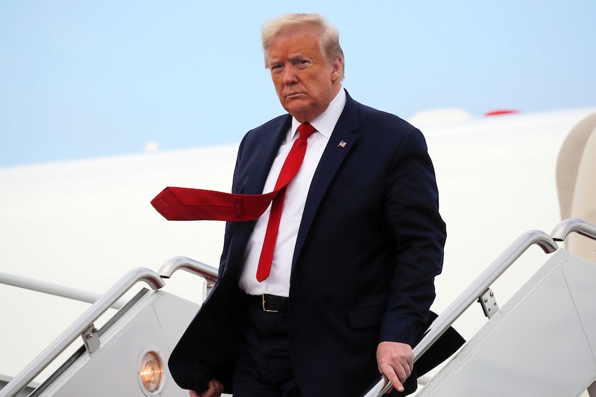 Donald Trump looks towards the camera scowling as he decends the plane stairs.