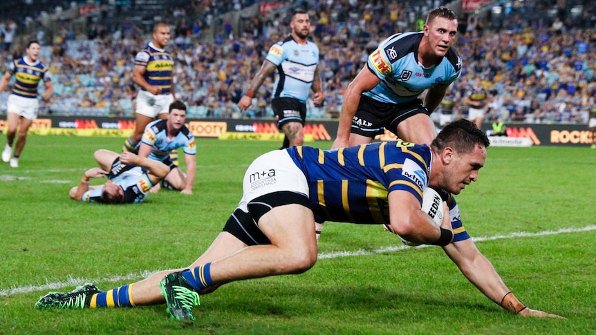 NRL player dives over for a try as a defender can only watch.