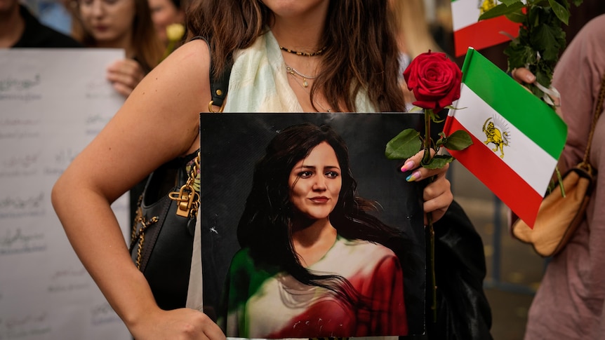 A woman holds an artistic depiction of Mahsa Amini.