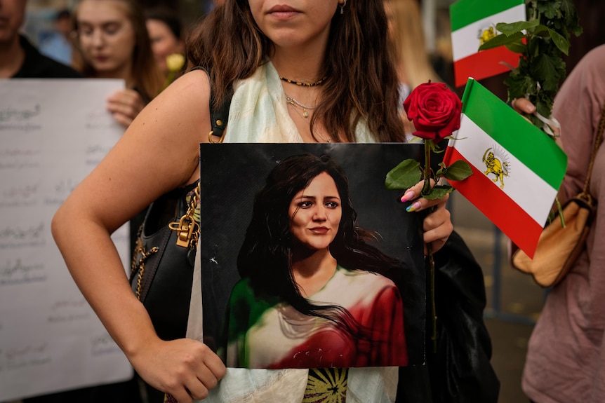 A woman holds an artistic depiction of Mahsa Amini.