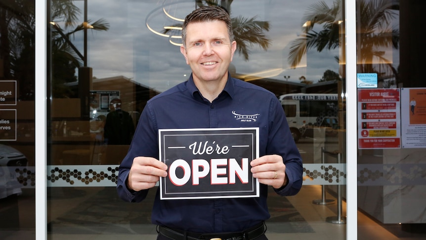 Man in blue shirt holding an open sign