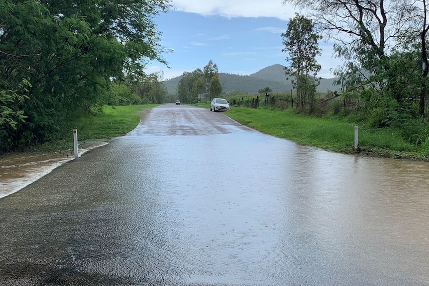 A street is flooded and two cars are parked on the other side of the water.