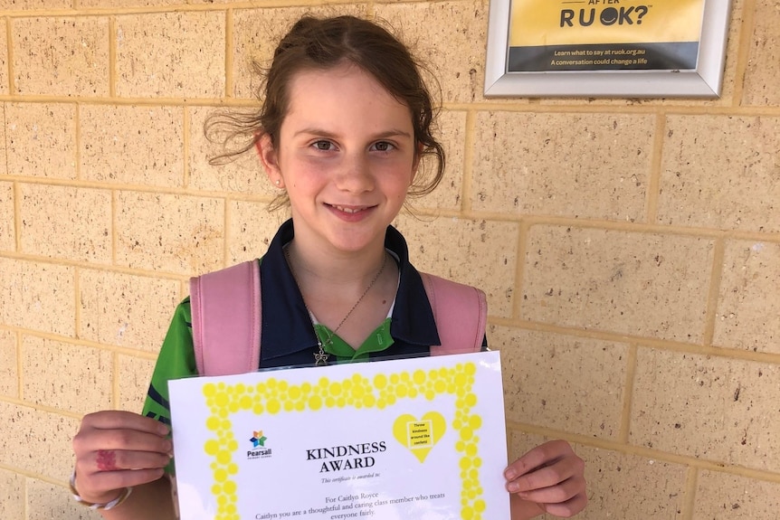 Caitlyn Royce holding a kindness certificate awarded to her at school.