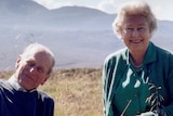 The Queen and Prince Philip pose for a photo at the top of a grassy hill.