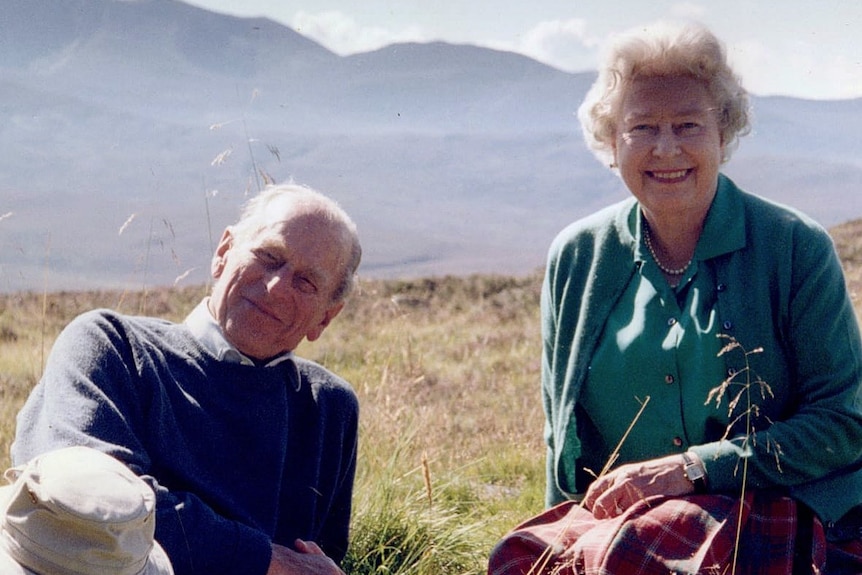 The Queen and Prince Philip pose for a photo at the top of a grassy hill.