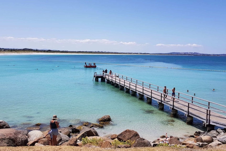 A beach setting with clear blue water, people swimming and sunshine.