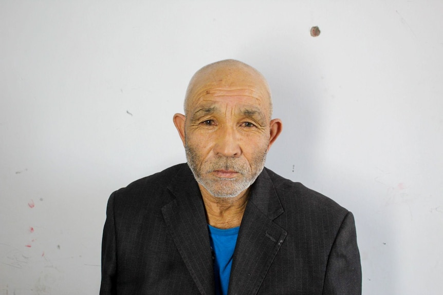 Omer Yunus, an older man with a shaved head, stares unsmiling at camera.