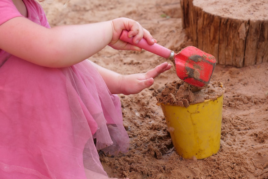 a child shovels sand into a plastic bucket 
