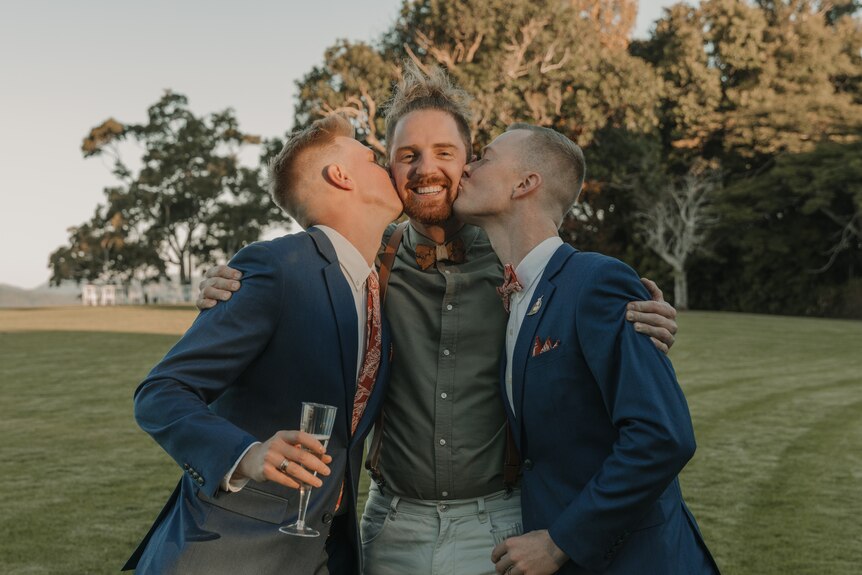 A man is kissed on the cheeks by two grooms.