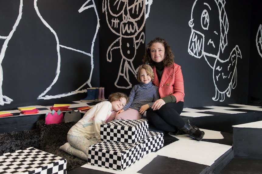 A woman and two little girls sit on a giant chess set.