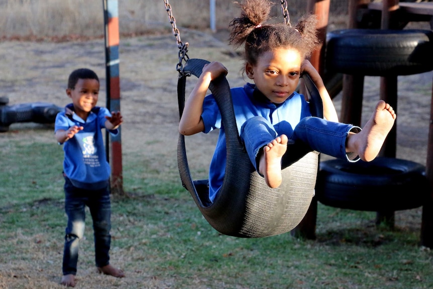 A young African boy pushes a girl on a swing.