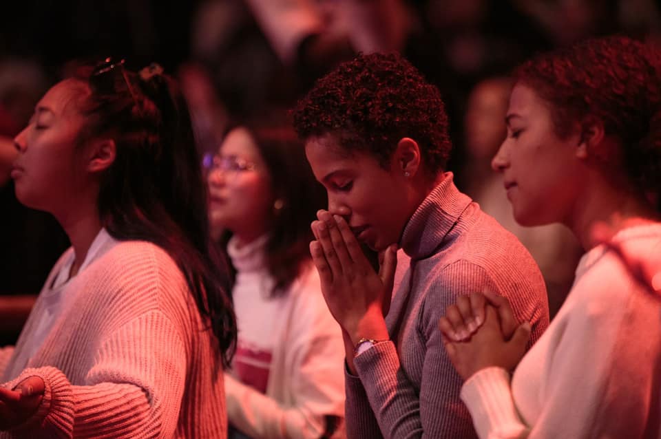 A red shadow is cast over women in a dark room during a church service 