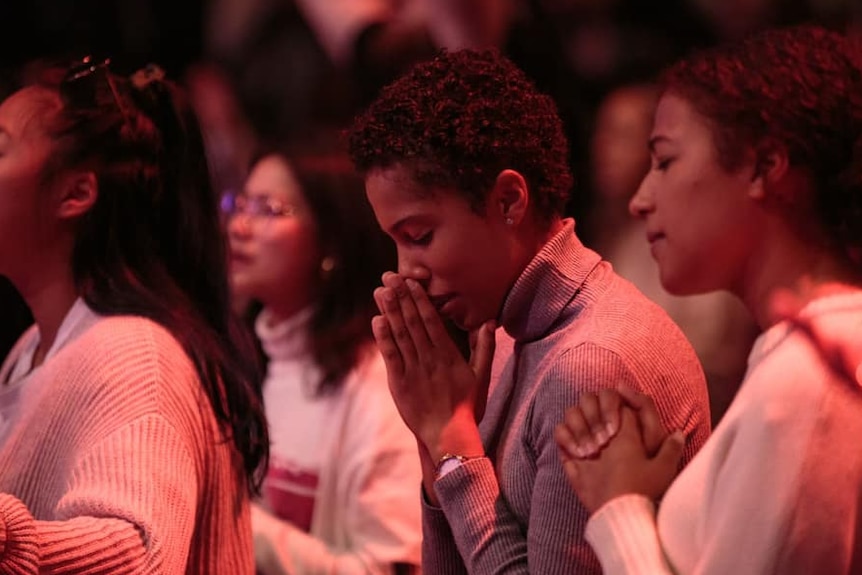 A red shadow is cast over women in a dark room during a church service 