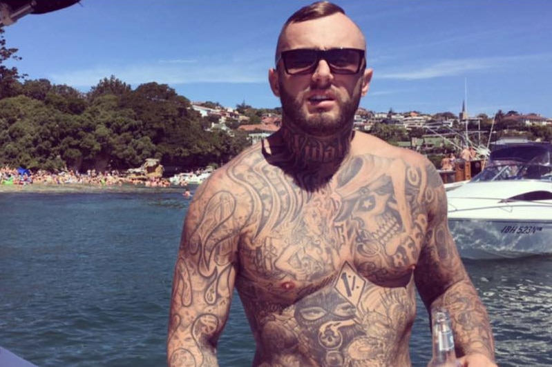 A heavily tattooed shirtless Michael Davey on a boat on the harbour.