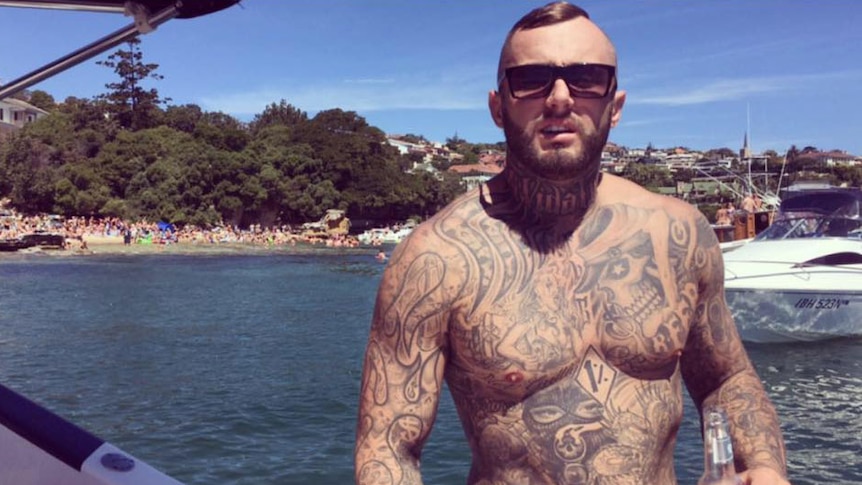 A heavily tattooed shirtless Michael Davey on a boat on the harbour.