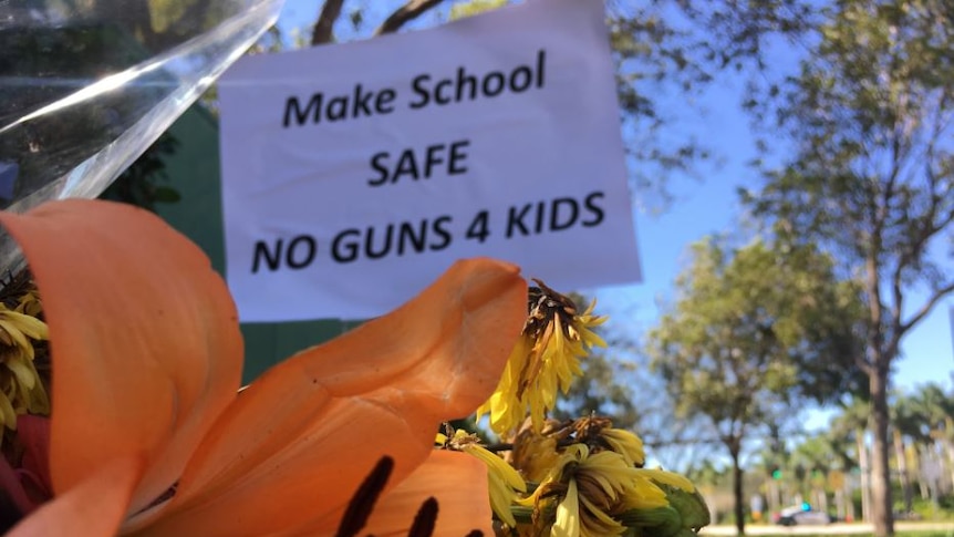 A sign behind a floral tribute says 'make school safe no guns 4 kids'