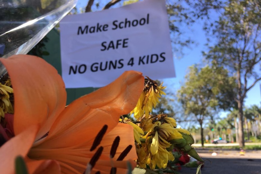 A sign behind a floral tribute says 'make school safe no guns 4 kids'