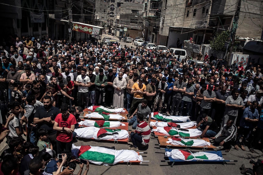 A large crowd of Palestinians surround eight dead bodies wrapped in the Palestinian flag at a funeral in the street in Gaza City