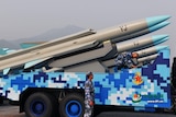 The missiles sit on a blue and white truck, they are grey with a blue tip, they have 'YJ' printed on them in black.