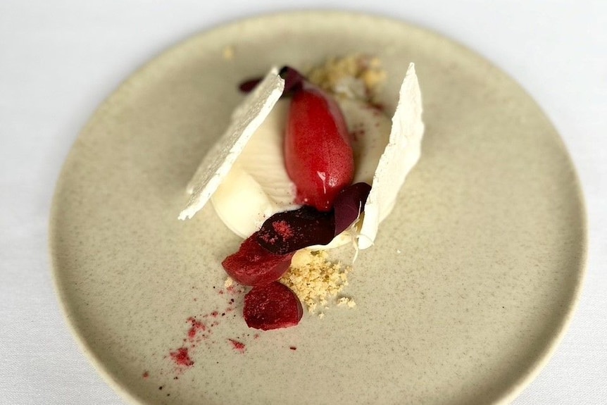 Two thin slices of meringue with a blob of cheese cake, a spoon of sorbet and dehydrated plum on a plate.