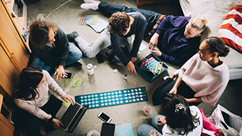 Teenagers circled around a board game on the carpet.