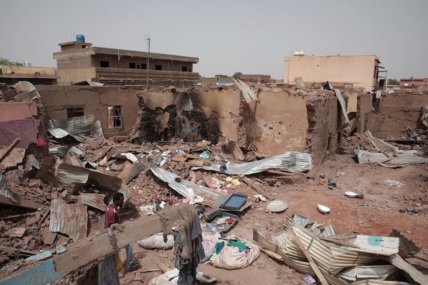 A man walks by the ruins of a destroyed house, with wreckage spread across a street.