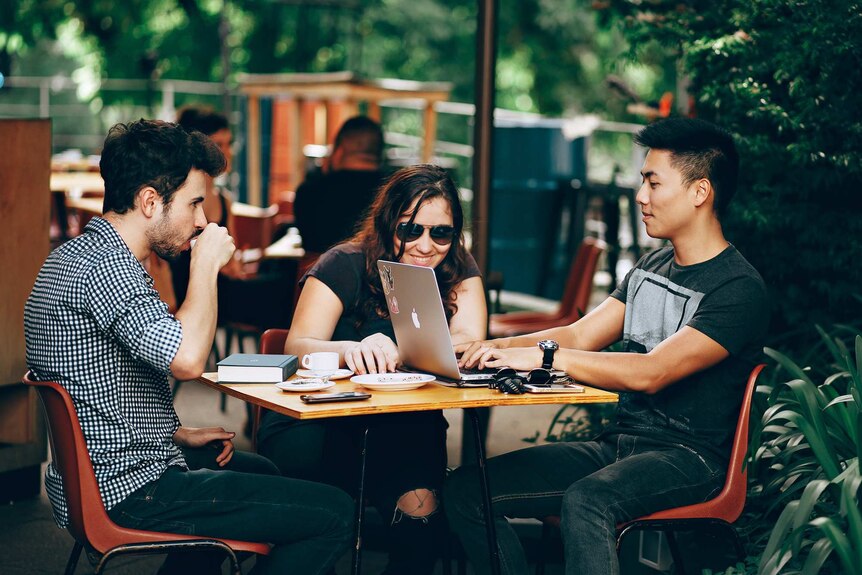 Two men and a woman having a meeting in an outdoor cafe setting for a story about creating a mentally healthy workplace.